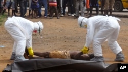 FILE - Health workers place the body of a man, whom they suspect of dying of the Ebola virus, inside a plastic body bag as a small crowd watches in Monrovia, Liberia, Sept. 4, 2014. 