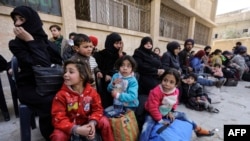 A picture taken on March 13, 2018 shows evacuated civilians and children sitting in the yard of a school lying on the government side of the Wafideen checkpoint on the outskirts of the Syrian capital Damascus neighboring the Eastern Ghouta enclave.