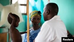 Three-year-old Eme Mbisa, who has a measles infection, rests her hand on the shoulder of her mother, Marianne Mbisa, as she talks to a doctor in northern Democratic Republic of Congo February 29 , 2020. (REUTERS/Hereward Holland)