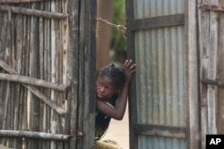 A young girl takes a look outside a gate near a site where two houses were crushed by the collapse of a massive, sprawling dumpsite in Pemba, Mozambique, April 29, 2019.