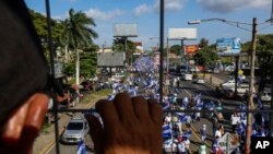 An individual watches from above as people march in an anti-government protest in Managua, Nicaragua, Aug. 11, 2018. The current unrest began in April, when President Daniel Ortega imposed cuts to the social security system and small protests by senior citizens were violently broken up. From then, more than 300 persons have died and demonstrators have demanded that Ortega leave power. 