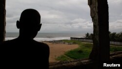 FILE - A young boy looks out from the window of his dilapidated home on the beach facing the Atlantic Ocean where his family lives in Monrovia, Liberia.