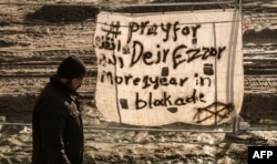 FILE - A man walks past a banner reading "Pray for Deir Ezzor" at the migrant camp known as the "Jungle" in Calais, France, Dec. 7, 2015.