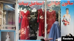 FILE - A woman wearing a burqa walks past a women's clothing store with headless mannequins displayed in its window, in Kabul, Afghanistan, Oct. 19, 2021.