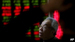 A man chats with other investors near an electronic board displaying stock prices at a brokerage house in Beijing, Jan. 5, 2016. 