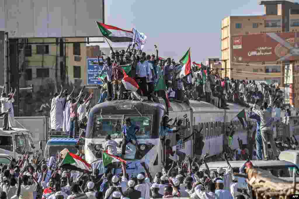 Sudanese protesters from the city of Atbara, sitting atop a train, arrive at the Bahari station in Khartoum. Many protesters perched on the roof of the train, waving Sudanese flags as it chugged through north Khartoum&#39;s Bahari railway station before winding its way to the protest site, an AFP photographer said.