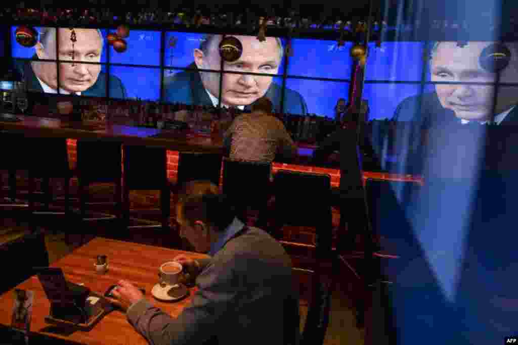 A man drinks coffee in front of screens broadcasting Russian President Vladimir Putin&#39;s yearly press conference, at a bar in Moscow, Russia.