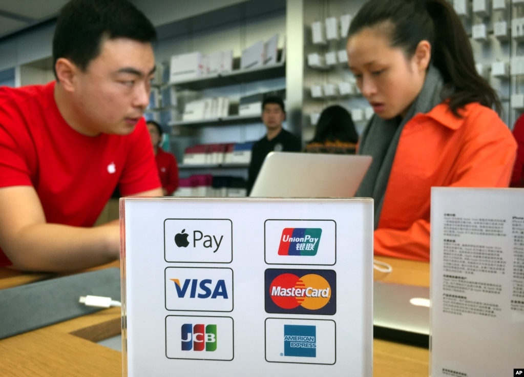 北京一家苹果专卖店的雇员和顾客谈话，旁边的纸板上显示了各种支付方式，包括苹果支付（2016年2月18日）。中国是苹果在美国以外最大的市场。2017年7月30日， &ldquo;泰晤士报&rdquo;报道，这是中国第一次成功利用它对苹果之类的国外重大技术平台的影响力，向软件制造商显示力量。