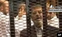 Video broadcast on Egyptian State Television shows ousted President Mohammed Morsi speaking from inside a mesh cage as he stands with other defendants during a court hearing at a police academy compound in Cairo, Egypt, Nov. 4, 2013.