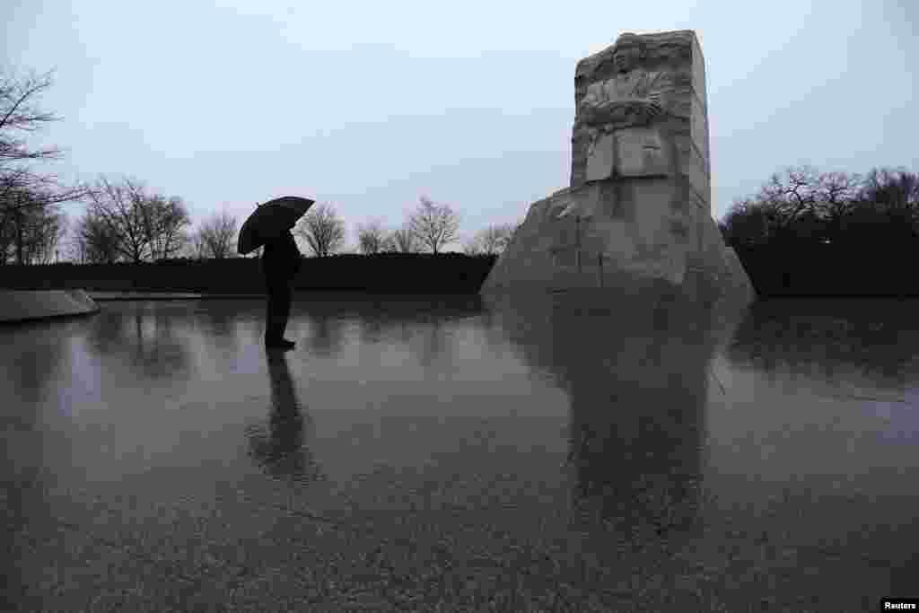 Di bawah payung dan hujan yang tak kunjung henti, seorang warga AS memberi penghormatan di Memorial Martin Luther King, Jr. di Washington (18/1). ​(Reuters/Jonathan Ernst)