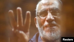 FILE - The Brotherhood's Supreme Guide Mohamed Badie waves with the Rabaa sign, symbolizing the support of the Muslim Brotherhood, as he stands behind bars during his trial with ousted Egyptian president Mohamed Morsi and other leaders of the Muslim Broth