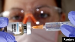 Seorang tenaga medis memegang botol kecil dengan stiker bertuliskan "Vaksin Covid-19" dan suntikan dalam foto ilustrasi, 10 April 2020. (Foto: Reuters)