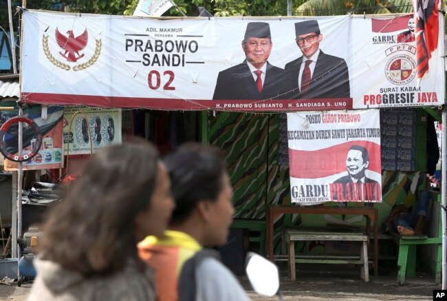 FILE - A couple rides a motorcycle past a campaign banners for Indonesian presidential candidate Prabowo Subianto, left, and his running mate Sandiaga Uno in Jakarta, Indonesia, Jan. 17, 2019.