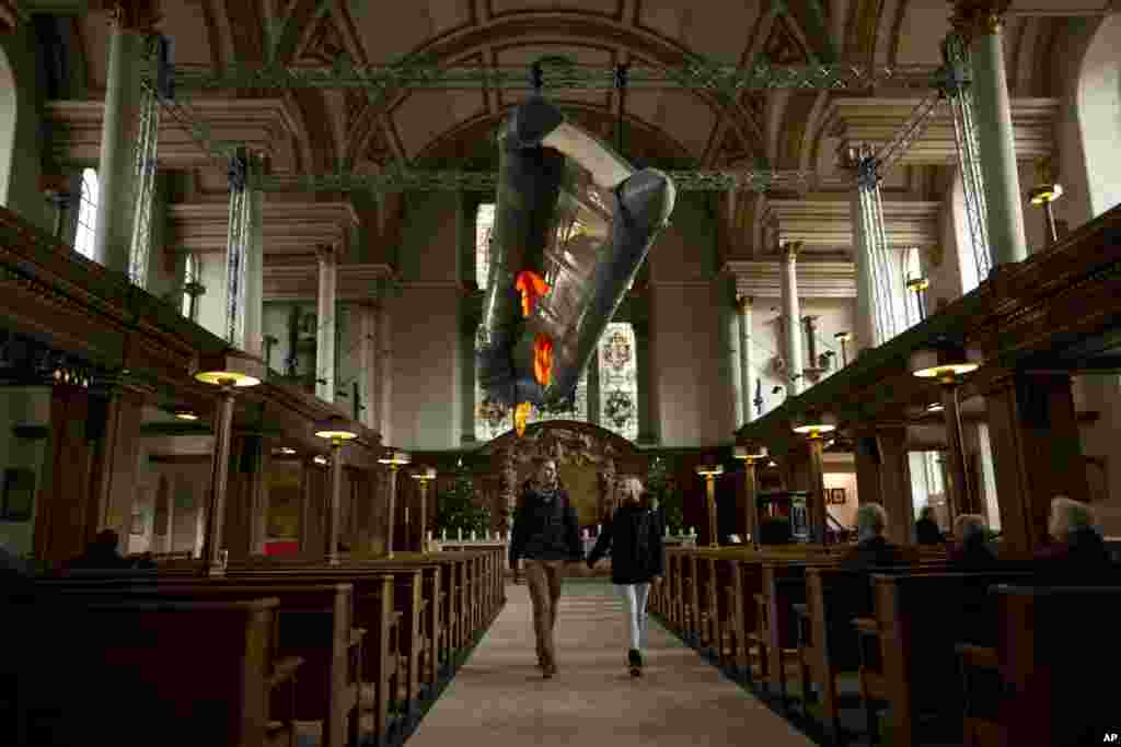 Tourists walk holding hands together beneath a salvaged dinghy with three life jackets-&nbsp;an installation entitled &#39;Flight&#39; by artist Arabella Dorman - hanging in the nave of St. James&rsquo;s Church, Piccadilly, in London.