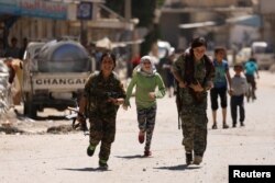 Syrian Democratic Forces female fighters run with children in the town of Tabqa, Syria, after SDF captured it from Islamic State militants this week, May 12, 2017.