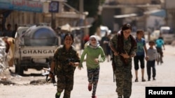 FILE - Syrian Democratic Forces female fighters run with children in the town of Tabqa, Syria, after SDF captured it from Islamic State militants in May 2017.