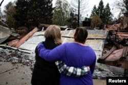 FILE - Irma Corona, right, comforts neighbor Gerryann Wulbern in front of the remains of Wulbern's home after the two returned for the first time since the Camp Fire in Paradise, Calif., Nov. 22, 2018.