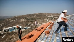 FILE - Men work on the roof of a house under construction in the unauthorized Jewish settler outpost of Havat Gilad, south of the West Bank city of Nablus, Nov. 2013. 