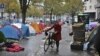 Seorang perempuan berjalan membawa sepedanya melewati tenda-tenda yang dibangun oleh para migran di Paris, Prancis, pada 4 November 2016. (Foto: AP/Thibault Camus)