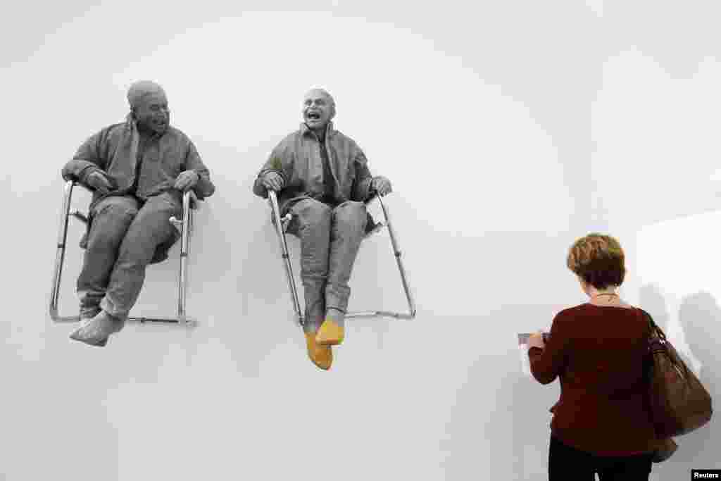 A visitor looks at "2 Seated on the Wall with Big Chairs" art works by artist Juan Munoz during the International Contemporary Art Fair at the Grand Palais in Paris, France.