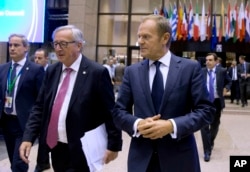 FILE - European Commission President Jean-Claude Juncker, center left, and European Council President Donald Tusk, center right, walk through the atrium during an EU summit in Brussels Oct. 19, 2017.
