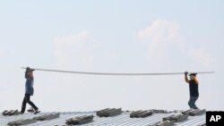 Workers carry a new tile while repairing the roof of an apartment building under the hot sun Sunday, April 27, 2014 in Bangkok, Thailand.