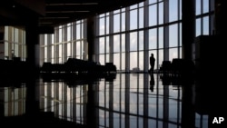 FILE - In this June 1, 2020 file photo, a woman looks through a window at a near-empty terminal at an airport in Atlanta. A new survey found that the coronavirus pandemic has taken a harsh toll on the mental health of young Americans. (AP Photo/Charlie Riedel, File)