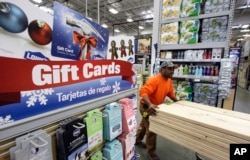 FILE - Contractor Greg Privitt pushes a cart of lumber past a display for gift cards at a Lowe's home improvement store in Seattle.