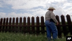 FILE -In this Sept. 16, 2015, photo, farmer Fausto Salinas stands along the border fence, in McAllen, Texas. The staggered fence or “wall,” costing $6.5 million per mile, runs along some 100 miles of Texas’ 1,254-mile border with Mexico. 