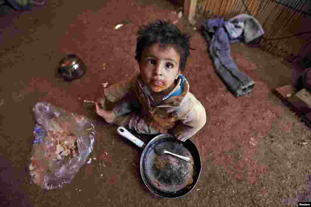 A young Syrian refugee eats inside his family&#39;s tent at an informal settlement in Deir al-Ahmar, Bekaa valley, Lebanon.