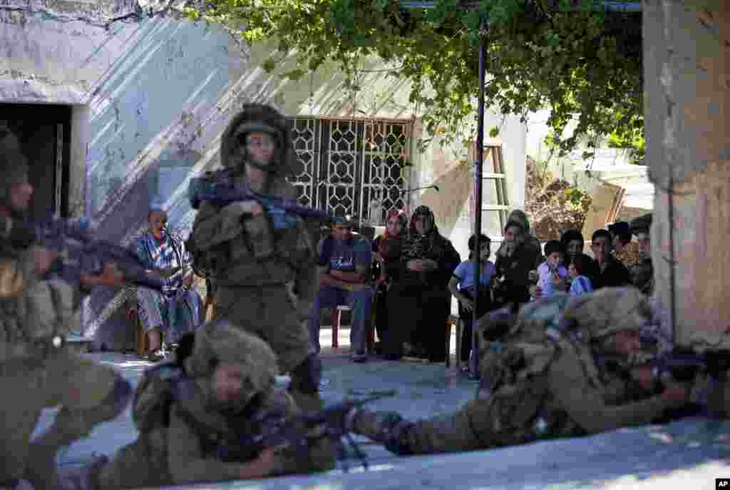 A Palestinian family looks at Israeli soldiers during a military operation searching for three missing teenagers, near the West Bank city of Hebron, June 15, 2014.