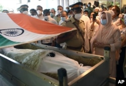 A police officer places an Indian national flag over the coffin of Bollywood icon Dilip Kumar during his funeral in Mumbai, India, Wednesday, July 7, 2021. (Kunal Patil/Pool photo via AP)