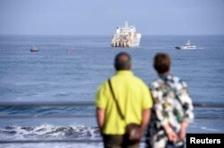 FILE - A couple observe a cable-laying ship at Arrietara beach, near Bilbao, northern Spain, June 13, 2017, as Facebook Inc. and Microsoft Corp. join forces to build an underwater fiber-optic cable across the Atlantic Ocean, linking Europe and the U.S.