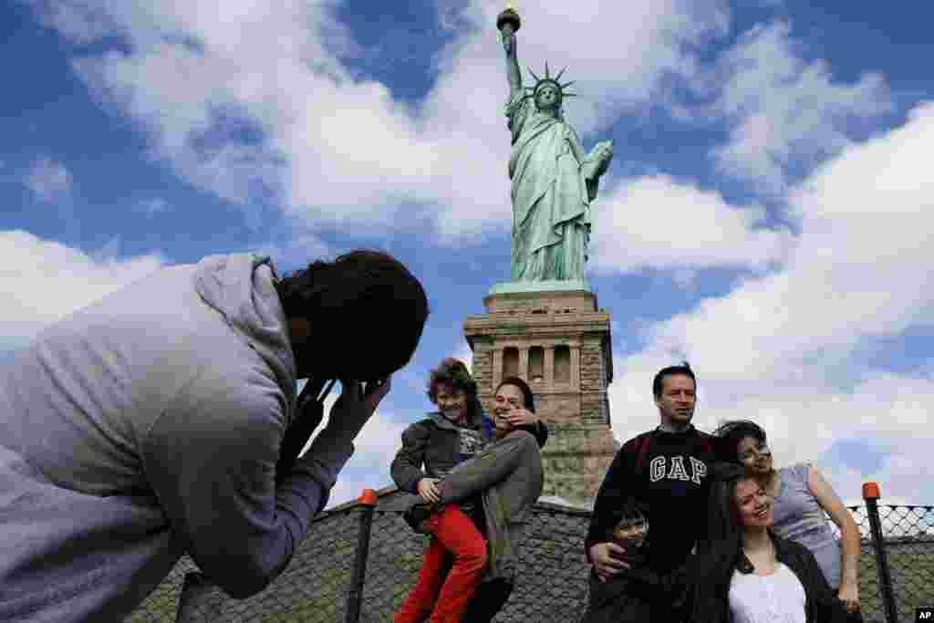 Tourists pose for photographs in front of the Statue of Liberty in New York Harbor in New York, Oct. 13, 2013. The Statue of Liberty reopened to the public after the state of New York agreed to shoulder the costs of running the site during the partial federal government shutdown.