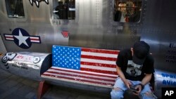 FILE - A man browses his smartphone on a bench decorated with a U.S. flag, outside a fashion boutique selling U.S. brand clothing at a shopping mall in Beijing, China, May 13, 2019.