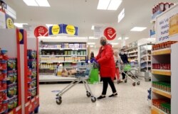 FILE - A woman wearing a face mask pushes a shopping cart at a Tesco supermarket in Hatfield, Britain, Oct. 6, 2020.