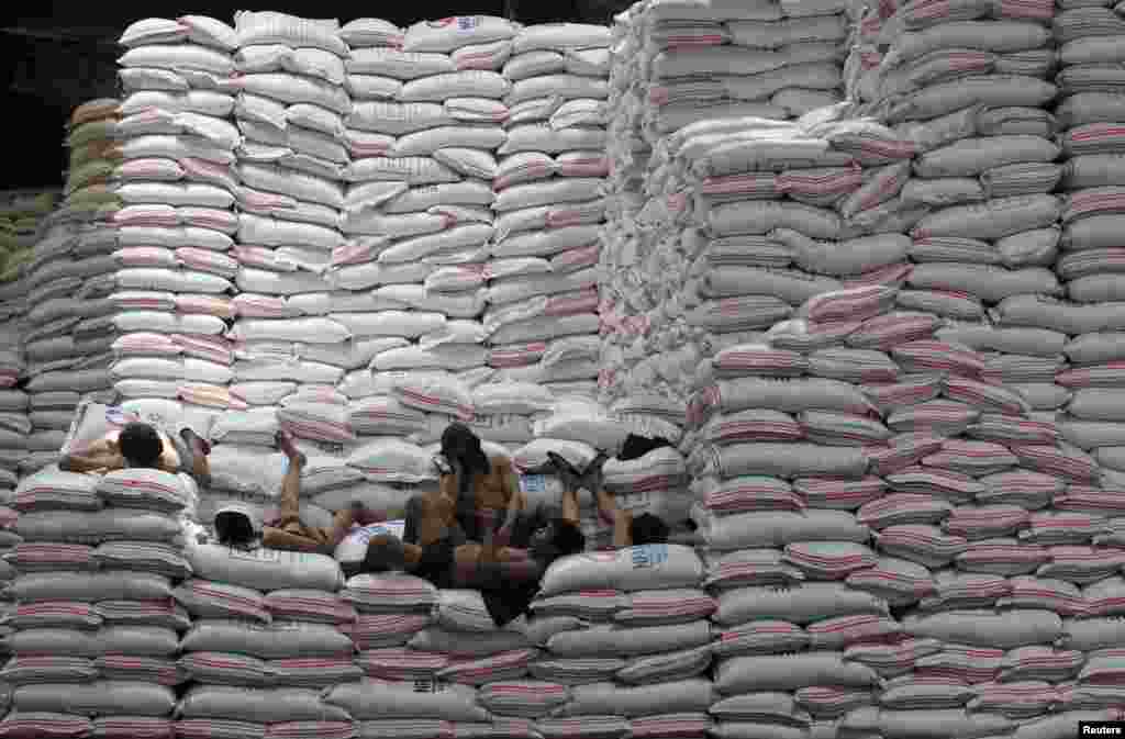 Para pekerja beristirahat di atas karung beras yang ditumpuk di depan gudang Otorita Makanan Nasional (NFA) di kota Taguig, Manila selatan, Filipina.