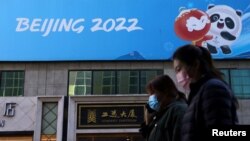 FILE - People walk past a banner for the Beijing 2022 Winter Olympic Games in Beijing, Oct. 27, 2021.