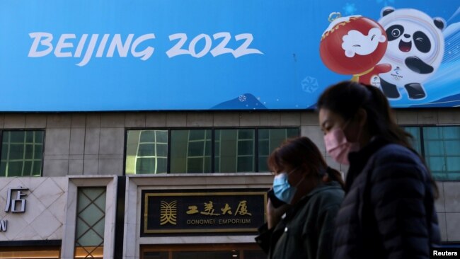 FILE - People walk past a banner for the Beijing 2022 Winter Olympic Games in Beijing, Oct. 27, 2021.