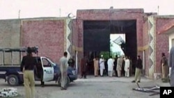 Police officers and people stand near a damaged jail gate after inmates escaped from the prison in the town of Bannu, Pakistan, in this still image taken from video, April 15, 2012.