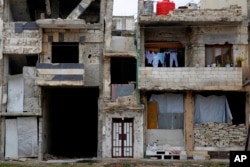 A family that returned to live in their apartment inside a heavily damaged building hang their clothes on a balcony in the Bab Dreib neighborhood of Homs, Syria, Jan. 17, 2018.