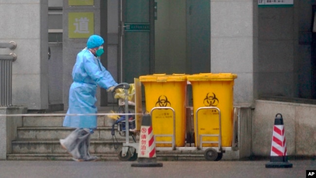 身穿防护服的工人推着医疗垃圾桶走过武汉医疗中心大门。（2020年1月22日）