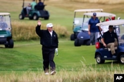 El presidente de Estados Unidos, Donald Trump, saluda a los manifestantes mientras juega golf en el Turnberry Golf Club, en Turnberry, Escocia, el sábado 14 de julio de 2018. Una docena de manifestantes organizaron un picnic de protesta en la playa frente al complejo.