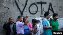 People wait in line next to the word "Vote" spray painted on a wall before voting during the Constituent Assembly election in Caracas, Venezuela, July 30, 2017. 