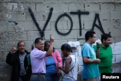 People wait in line next to the word "Vote" spray painted on a wall before voting during the Constituent Assembly election in Caracas, Venezuela, July 30, 2017.