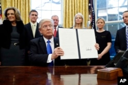President Donald Trump holds up a signed executive order in the Oval Office of the White House in Washington, Jan. 28, 2017.