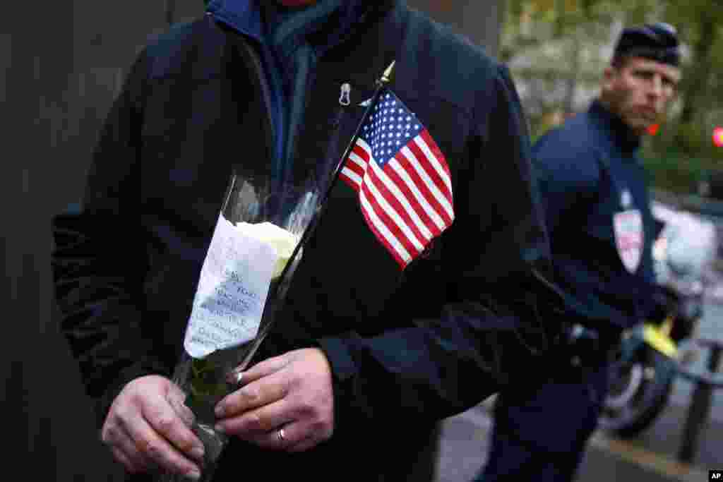 Seorang turis AS di Paris memberi penghormatan sebelah polisi Perancis di depan gedung konser Bataclan (13/11), setelah upacara untuk mengenang para korban serangan maut di ibukota Perancis itu tahun lalu yang menewaskan 130 orang. (AP/Francois Mori)