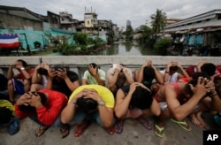 FILE - Filipino men place their hands over their heads as they are rounded up during a police operation as part of the continuing "War on Drugs" campaign of Philippine President Rodrigo Duterte in Manila, Philippines.