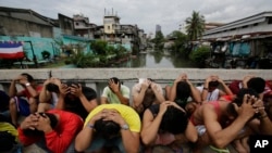 FILE - Filipino men place their hands over their heads as they are rounded up during a police operation as part of the continuing "War on Drugs" campaign of Philippine President Rodrigo Duterte in Manila, Philippines.