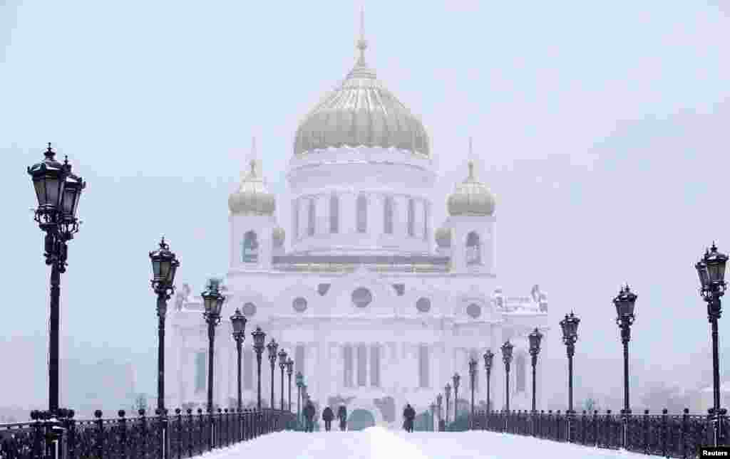 People walk along the Patriarchal Bridge over the Moskva river near the Cathedral of Christ the Saviour as it snows in central Moscow, Russia.